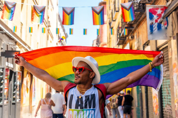 A gay black man walking wearing sunglasses at the pride party with an LGBT flag