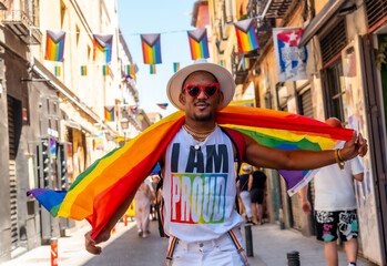 Black gay man walking wearing sunglasses at pride party with LGBT flag, smiling