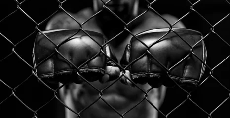Foto auf Acrylglas Black and white image of a man in a boxing cage. The concept of sports, Muay Thai, martial arts. © andy_gin