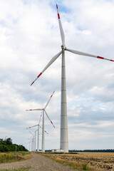 Fototapeta premium Towers of wind turbines with rotating blades at sunset against cloudy sky. Close-up. Adyghe wind farm from many towers of wind turbines in field. Wind power complex of Rosatom.