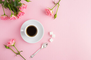 Coffee in the white cup and pink roses on the pink  background. Top view. Copy space.