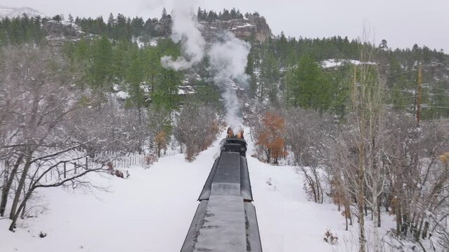 Aerial cinematic drone flying above moving steam train. Exciting railroad tour by old historic train carriages. Inspiring travel, tourists exploring winter forest on motivational adventure vacation 4K