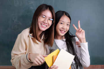 Portrait of young teacher embracing girl pupil posing to camera with smile in front of blackboard...