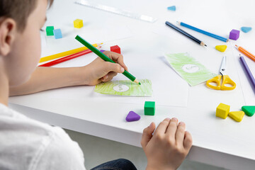 A little boy enthusiastically draws toy money with colored pencils for the game. Selective focus....