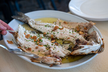 Serving in restaurant of fresh grilled on old charcoal parrillas sea bass fish in small fisherman's village Getaria, Basque Country, Spain