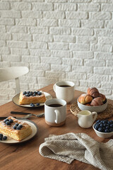 Still life in scandinavian style on a wooden kitchen table. Coffee, homemade cakes and fresh blueberries for breakfast. Concept for good morning wishes. Kinfolk style life. Copy space. Vertical photo
