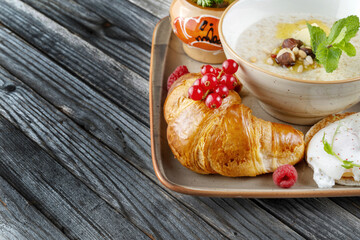 Breakfast. Fruits, croissants, porridge, poached eggs. On rustic dark wooden table.