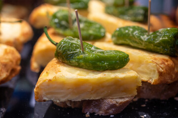 Typical snack in bars of Basque Country, pinchos or pinxtos, small slices of bread withn different toppings and fastened with skewers, San Sebastian, Spain. Potato tortilla with green pepper.