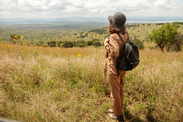 Back view of female tourist with black backpack enjoying the views of the savannah, copy space