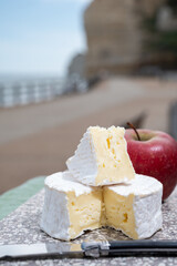 Tasting of round camembert cow cheese from Calvados region served with apple and view on alebaster cliffs Porte d'Aval in Etretat, Normandy, France