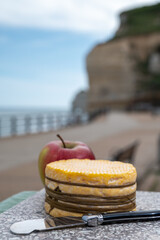 Tasting of yellow livarot cow cheese from Calvados region served with apple and view on alebaster cliffs Porte d'Aval in Etretat, Normandy, France