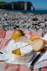 Lunch with french round camembert cow cheese from Calvados region, fresh baked baguette bread and apple on pebbles stones beach with view on alebaster cliffs Porte d'Aval in Etretat, Normandy, France