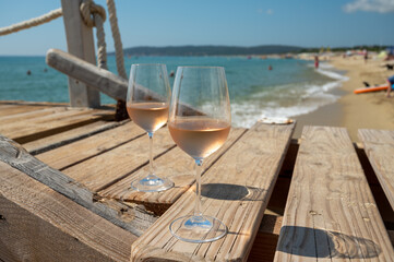 Glasses of cold rose wine from Provence served outdoor on wooden yacht pier with view on blue water and white sandy beach Plage de Pampelonne near Saint-Tropez, France