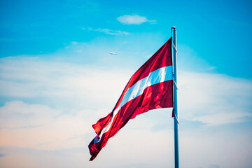 Flag of the Republic of Latvia. Latvian flag waving in the wind against the blue sky. - obrazy, fototapety, plakaty