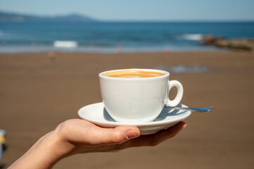 Drinking cappuccino coffee on Atlantic ocean with view on sandy beach