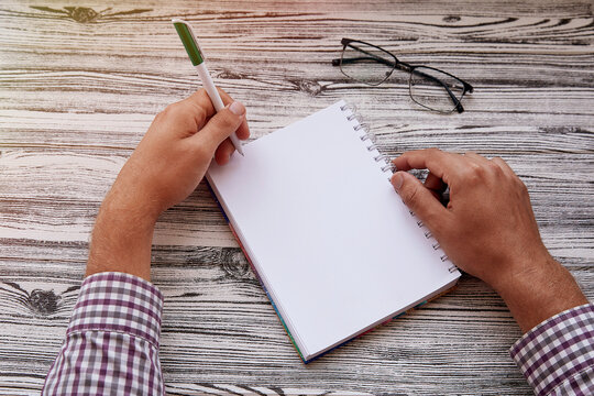 Man writing in notepad, using his left hand. Conceptual photo of lefthanded day. Mock up notepad. Top view. Copy space.