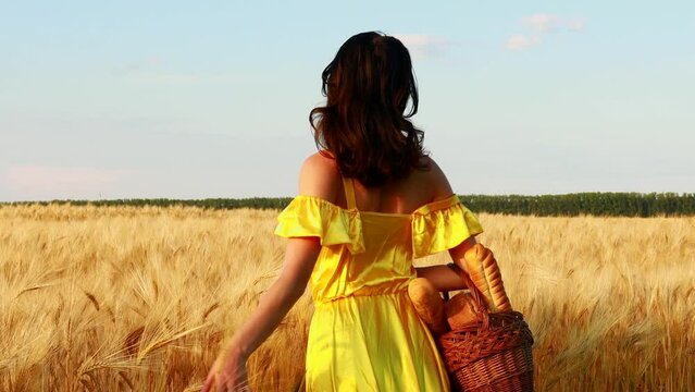 Young woman in yellow dress standing on a wheat field with sunrise on the background.