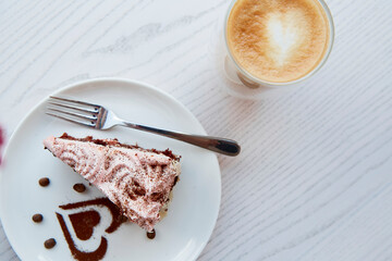 Fruit chocolate cake and a glass with a double bottom of latte on wooden table outside in the cafe terrace. Atmospheric breakfast. Heart shaped dessert decorations.