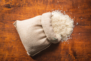 Fototapeta na wymiar Uncooked white rice in burlap sack on wooden table.