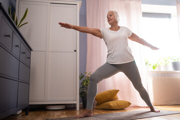 senior lady doing yoga asana at living room.
