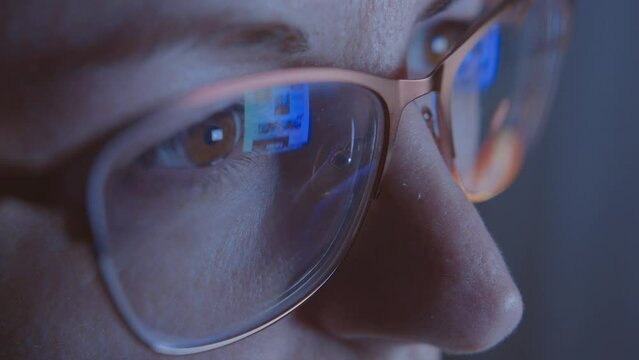 A woman with glasses in the evening works at the monitor screen, close-up, reflection in glasses