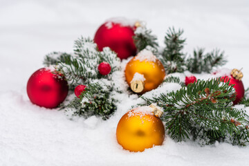 Close-up photo of the coniferous branches decorated with few big toys for the Christmas tree lying in the snow