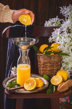 queezing orange fruit and making fresh orange juice . Still life with orange juice glass bottle placed with sliced oranges,  wooden squeezer and white flowers on rustic wooden chair.
