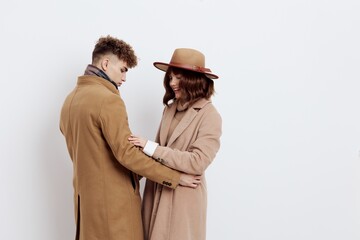 a cute couple is standing sideways on a light background dressed in coats and sweaters, hugging each other's hands