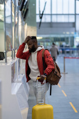 Upset depressed African American man with luggage standing at check-in counter in airport, being sad about moving away from home and family. Travel and depression, pre-travel anxiety