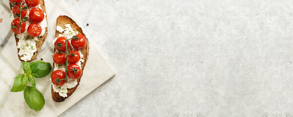 A sandwich with roasted cherry tomatoes with branch, fresh cottage cheese, green basil on a slice of whole wheat bread on a marble board on grey background