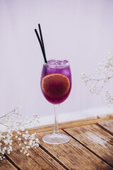 Stem wine glass with purple cocktail. Cocktail with orange and ice on a wooden table