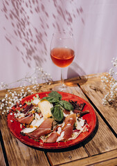Glass of rose wine and Salad with jamon, basil leaves and cheese on a plate. Plate with salad on wooden table