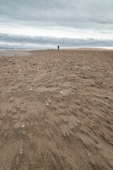 Vertical shot of a guy walking on the beach along the ocean in Ebro Delta, Spain