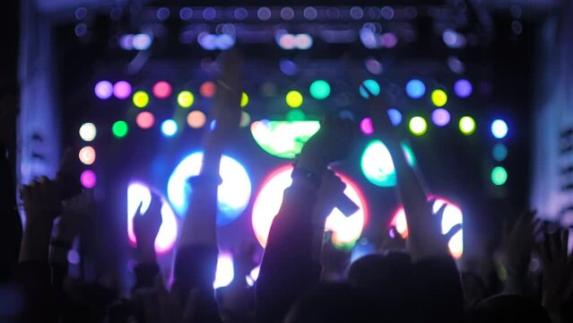People silhouettes partying, cheering, raising hands up and jumping at rock concert in front of stage of nightclub. Bright colorful stage lighting. Nightlife and entertainment concept