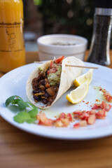 taco dish with vegetables and sauces, orange juice and sauce on the table