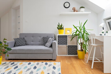 Interior of room teenager in the attic with white wall, desk and chair and modern sofa and carpet on wooden floor. Room children with yellow design and scandinavian style.