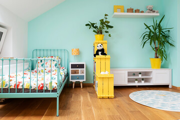Cozy room child for girl in pastel color in the attic in scandinavian design. Comfortable bed for kid with colorful bedding, bedside table and carpet on wooden floor. Yellow and turquoise color.