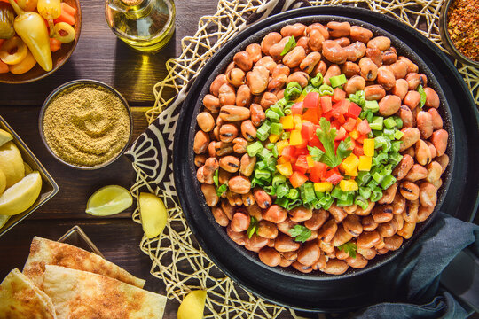Arabic Cuisine: Egyptian traditional dish "Ful medames". Middle Eastern breakfast with cooked fava beans and fresh vegetables. Served with olive oil, pickles, pita bread, cumin and lemon. 