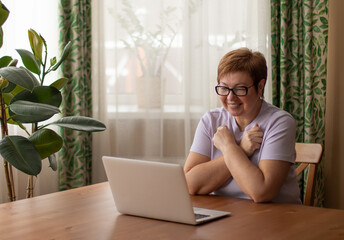 An adult woman sits at a laptop and communicates via video link in sign language. Shows a gesture...