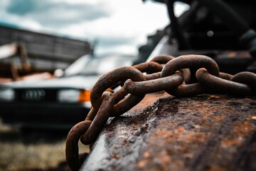 Closeup of an old iron chain on a rust surface with a car in the background