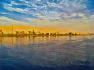 Fototapeta premium Along the Nile River in Egypt, with blue water, blue sky, and the bright white sail of a small boat. With a thin strip of greenery and dunes behind the line of green.