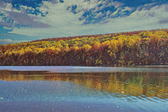 Sunny fall day at the Catoctin State Park, with the trees in full autumn foliage.  With a reflection of the golden leaves in the water.  Edited to create a painted image. 