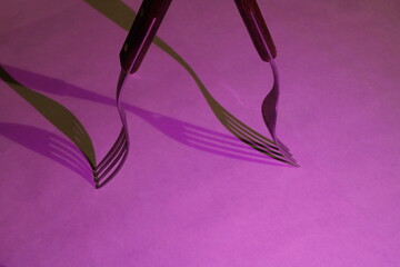 Los tenedores abiertos en ángulo con luces cruzadas proyectan sombras sobre las sombras en la superficie, presentan un diseño culinario abstracto original y hermoso con fondo magenta