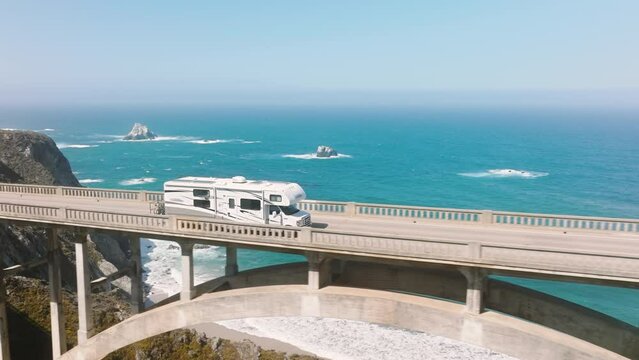Aerial RV driving by road on American road trip with cinematic ocean background. Scenic beautiful drone footage of famous Bixby bridge. Tourist exploring nature. Family vacation travel RV holiday trip