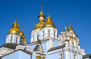 Fototapeta na wymiar Shiny golden cupolas of the St. Michaels Golden Domed Monastery on blue sky background. Kyiv, Ukraine