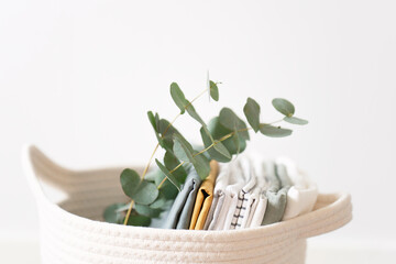 basket with home textiles in bright room close-up, and eucalyptus branch, organic cotton - obrazy, fototapety, plakaty