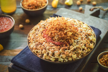 Arabic cuisine; Traditional Egyptian food:Delicious Kushary or Koushari of rice, pasta,chickpeas, lentils,crispy fried onions, fresh lemon and tomato garlic sauce on a plate. Close up with copy space.