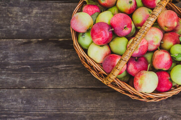 Harvest ripe apples in a wicker basket on a wooden background with space for text.