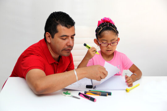 Latino dad and daughter, teacher and student draw in a notebook with colors in this back to school to improve skills with Autism Spectrum Disorder (ASD)
