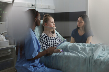 Girl with fractured neck discussing with mother while nurse examining injury. Daughter wearing...